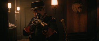 Movie still from “Violent Night” (2022), directed by Tommy Wirkola – A man in a uniform holding a gun in a dark room; Medium shot, Low angle
