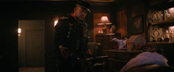 Movie still from “Violent Night” (2022), directed by Tommy Wirkola – A man in a uniform holding an object in his hands; Medium shot, Low angle