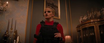 Movie still from “Violent Night” (2022), directed by Tommy Wirkola – A woman in a red shirt is standing in front of a painting; Medium shot, Low angle