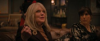 Movie still from “Violent Night” (2022), directed by Tommy Wirkola – An older woman sitting on top of a couch in a room; Close Up shot, Over the shoulder angle