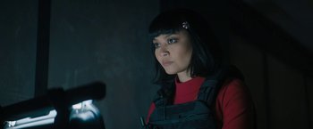 Movie still from “Violent Night” (2022), directed by Tommy Wirkola – A woman in a red shirt is looking at the camera; Close Up shot, Over the shoulder angle