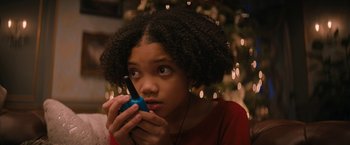 Movie still from “Violent Night” (2022), directed by Tommy Wirkola – A young girl holding a cell phone in front of a christmas tree; Close Up shot, High angle