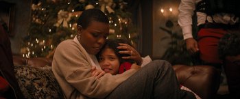Movie still from “Violent Night” (2022), directed by Tommy Wirkola – A woman sitting next to a young girl in front of a christmas tree; Close Up shot, High angle