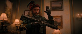 Movie still from “Violent Night” (2022), directed by Tommy Wirkola – A man dressed in costume holding a rifle; Medium shot, Over the shoulder angle