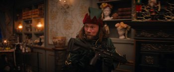 Movie still from “Violent Night” (2022), directed by Tommy Wirkola – A man with a beard wearing a hat and holding a rifle; Medium shot, Over the shoulder angle