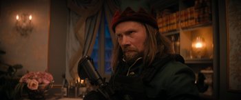 Movie still from “Violent Night” (2022), directed by Tommy Wirkola – A man with long hair and a beard wearing a red hat; Medium shot, Over the shoulder angle