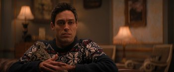 Movie still from “Violent Night” (2022), directed by Tommy Wirkola – A person sitting in a chair wearing a sweater; Close Up shot, Over the shoulder angle