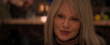 Movie still from “Violent Night” (2022), directed by Tommy Wirkola – An older woman with long blonde hair wearing a brown scarf; Close Up shot, Over the shoulder angle