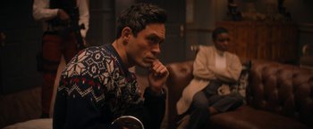 Movie still from “Violent Night” (2022), directed by Tommy Wirkola – A man sitting in a room next to another person; Medium shot, Over the shoulder angle