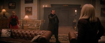 Movie still from “Violent Night” (2022), directed by Tommy Wirkola – A man standing in a living room holding a cell phone; Wide shot, Over the shoulder angle