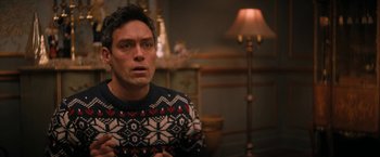 Movie still from “Violent Night” (2022), directed by Tommy Wirkola – A man wearing a sweater sitting in front of a lamp; Close Up shot, Over the shoulder angle