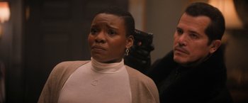 Movie still from “Violent Night” (2022), directed by Tommy Wirkola – An older woman with short black hair wearing a white shirt; Close Up shot, Over the shoulder angle