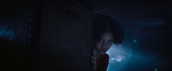 Movie still from “Violent Night” (2022), directed by Tommy Wirkola – A young girl is peeking out from behind a wall; Close Up shot, Low angle