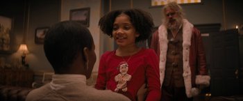 Movie still from “Violent Night” (2022), directed by Tommy Wirkola – A young girl wearing a gingerbread man necklace; Medium shot, Over the shoulder angle