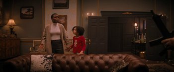 Movie still from “Violent Night” (2022), directed by Tommy Wirkola – A woman standing next to a young girl in front of a couch; Medium shot, Over the shoulder angle