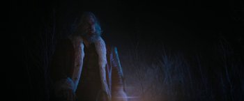 Movie still from “Violent Night” (2022), directed by Tommy Wirkola – A man with a long beard wearing a white fur coat; Medium shot, Over the shoulder angle