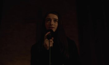 Movie still from “Vox Lux” (2018), directed by Brady Corbet – A person holding a microphone in a dark room; Close Up shot, Low angle