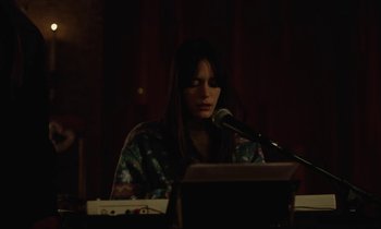 Movie still from “Vox Lux” (2018), directed by Brady Corbet – A person sitting at a table with a microphone; Medium shot, Over the shoulder angle