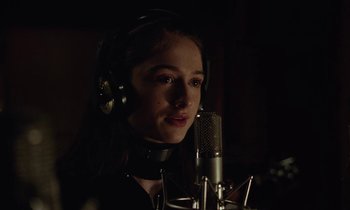 Movie still from “Vox Lux” (2018), directed by Brady Corbet – A young girl wearing headphones is recording a song; Close Up shot, Over the shoulder angle