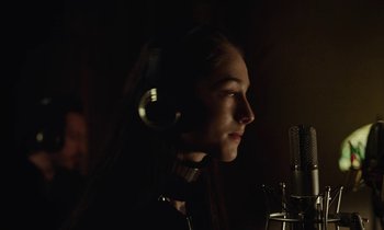 Movie still from “Vox Lux” (2018), directed by Brady Corbet – A woman wearing headphones is recording a song; Close Up shot, Over the shoulder angle