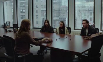 Movie still from “Vox Lux” (2018), directed by Brady Corbet – A group of people sitting around a table in front of a window; Medium shot, Over the shoulder angle