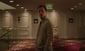 Movie still from “Vox Lux” (2018), directed by Brady Corbet – A man standing in an empty room in front of a sign; Medium shot, Low angle