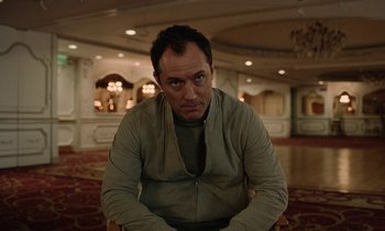 Movie still from “Vox Lux” (2018), directed by Brady Corbet – A man sitting in front of a mirror in a room; Medium shot, Low angle