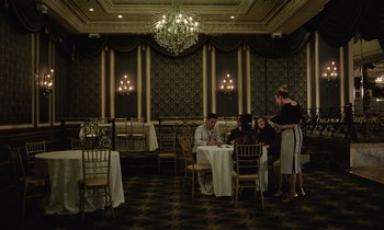 Movie still from “Vox Lux” (2018), directed by Brady Corbet – A group of people sitting at a table in a restaurant; Extreme Wide shot, High angle