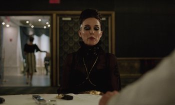 Movie still from “Vox Lux” (2018), directed by Brady Corbet – A woman sitting at a dinner table wearing a black dress; Medium shot, Over the shoulder angle