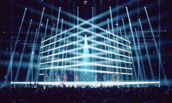 Movie still from “Vox Lux” (2018), directed by Brady Corbet – A group of people standing on top of a stage under lights; Extreme Wide shot, Low angle