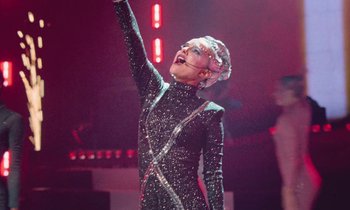 Movie still from “Vox Lux” (2018), directed by Brady Corbet – A woman in a black outfit raising her hand; Medium shot, Low angle