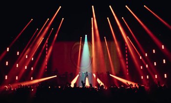 Movie still from “Vox Lux” (2018), directed by Brady Corbet – A person is standing in the middle of a stage with lights; Extreme Wide shot, Low angle