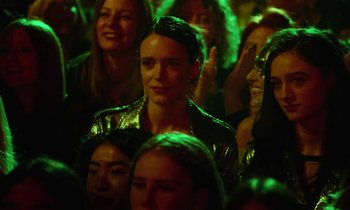 Movie still from “Vox Lux” (2018), directed by Brady Corbet – A group of people sitting in a room with green lights; Close Up shot, Over the shoulder angle