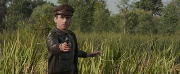 Movie still from “Welcome to Marwen” (2018), directed by Robert Zemeckis – A man in a field holding a gun pointing to the ground; Medium shot, Over the shoulder angle