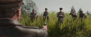 Movie still from “Welcome to Marwen” (2018), directed by Robert Zemeckis – A group of men standing next to each other in the grass; Wide shot, Over the shoulder angle