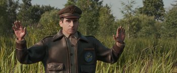 Movie still from “Welcome to Marwen” (2018), directed by Robert Zemeckis – A man in a military uniform standing next to some tall grass; Medium shot, Over the shoulder angle