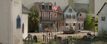 Movie still from “Welcome to Marwen” (2018), directed by Robert Zemeckis – An american flag flies in front of a building; Extreme Wide shot, High angle
