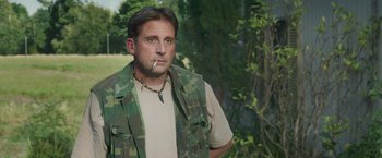 Movie still from “Welcome to Marwen” (2018), directed by Robert Zemeckis – A man in a camouflage vest is smoking a cigarette; Medium shot, High angle