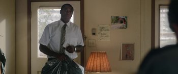 Movie still from “Welcome to Marwen” (2018), directed by Robert Zemeckis – A man in a white dress shirt and tie holding a bag of garbage; Medium shot, Low angle
