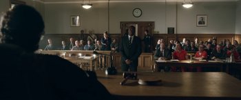 Movie still from “Welcome to Marwen” (2018), directed by Robert Zemeckis – A man standing in front of a courtroom filled with people; Wide shot, Over the shoulder angle