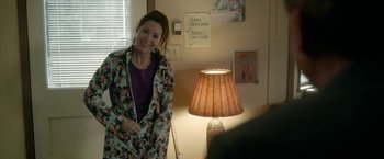 Movie still from “Welcome to Marwen” (2018), directed by Robert Zemeckis – A woman standing next to a lamp in a living room; Medium shot, Over the shoulder angle