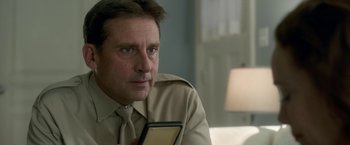 Movie still from “Welcome to Marwen” (2018), directed by Robert Zemeckis – A person wearing a suit and tie holding a cell phone; Close Up shot, Over the shoulder angle