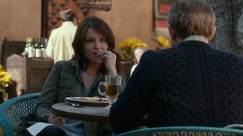 Movie still from “Whiskey Tango Foxtrot” (2016), directed by Glenn Ficarra – A woman sitting at a table with a plate of food; Medium shot, Over the shoulder angle