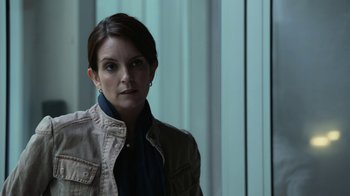 Movie still from “Whiskey Tango Foxtrot” (2016), directed by Glenn Ficarra – A woman in a brown jacket standing in front of a window; Close Up shot, Over the shoulder angle