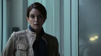 Movie still from “Whiskey Tango Foxtrot” (2016), directed by Glenn Ficarra – A woman in a brown jacket standing in front of a window; Close Up shot, Over the shoulder angle