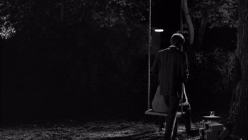 Movie still from “Who's Afraid of Virginia Woolf?” (1966), directed by Mike Nichols – A man standing next to a swing at night; Wide shot, Over the shoulder angle