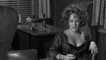 Movie still from “Who's Afraid of Virginia Woolf?” (1966), directed by Mike Nichols – A woman sitting at a table with a glass of wine; Medium shot, Over the shoulder angle