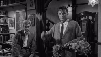 Movie still from “Who's Afraid of Virginia Woolf?” (1966), directed by Mike Nichols – A man holding a bouquet of flowers while standing next to another man in a suit; Medium shot, Over the shoulder angle