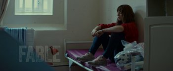Movie still from “Wild Rose” (2018), directed by Tom Harper – A woman sitting on a bed in a room; Medium shot, Over the shoulder angle