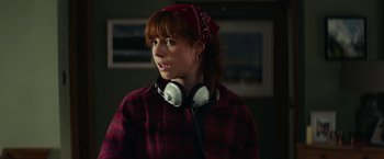 Movie still from “Wild Rose” (2018), directed by Tom Harper – A woman wearing a red bandana and plaid shirt with headphones on; Close Up shot, Over the shoulder angle